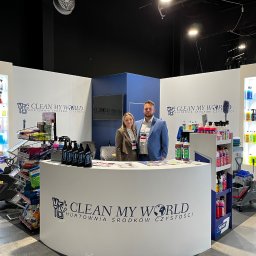 Clean My World - Stoisko targowe firmy Clean My World z ekspozycją środków czystości, mopów i wózków. Dwie osoby za ladą. Targi Warsaw CleanTech Expo. Oświetlenie punktowe.