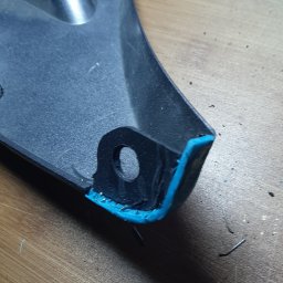 Lamintech - Naprawiony element z tworzywa sztucznego z widocznym spawem, wzmocniony niebieskim tworzywem. Detal z otworem montażowym na drewnianym blacie.