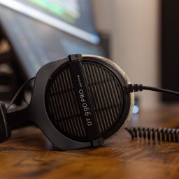 Miłosz Tuszyński - Baga Sound - Profesjonalne słuchawki studyjne DT 990 PRO 250 Ohm na drewnianym biurku, z widocznym kablem spiralnym i fragmentem monitora w tle. Sprzęt audio dla studia.