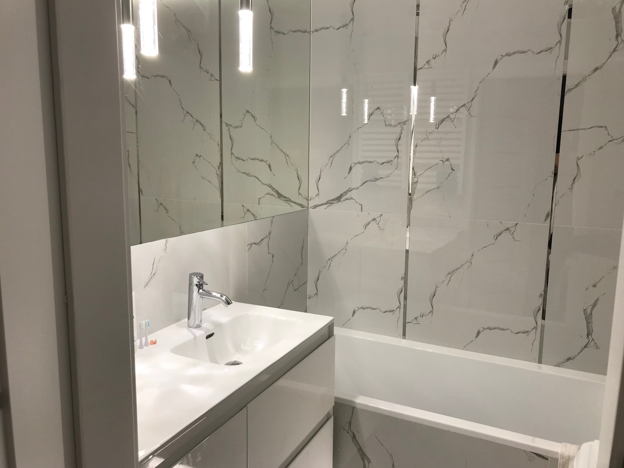 Biała łazienka z marmurowymi płytkami, chromowaną armaturą i podświetlanym lustrem. Nowoczesny design z minimalistycznym akcentem.