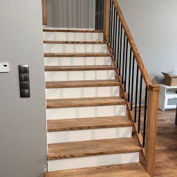 FRWD SPÓŁKA Z OGRANICZONĄ ODPOWIEDZIALNOŚCIĄ - Drewniane schody z białymi podstopnicami i czarnymi balustradami, widok z dołu. Naturalne oświetlenie, parkiet na podłodze. Detal wykończenia wnętrza.