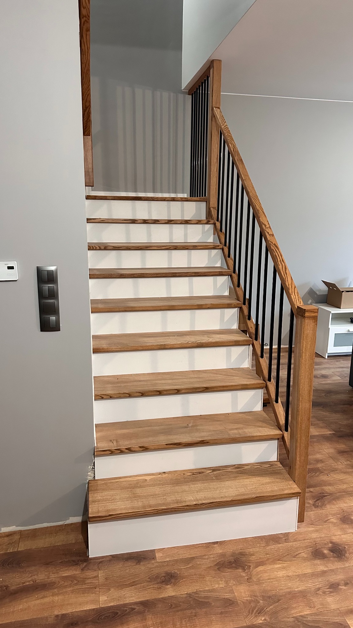 Drewniane schody z białymi podstopnicami i czarnymi balustradami, widok z dołu. Naturalne oświetlenie, parkiet na podłodze. Detal wykończenia wnętrza.