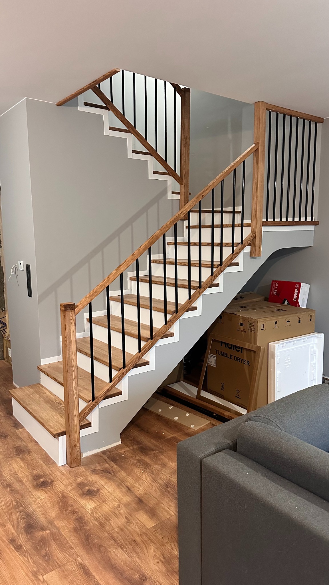 Nowoczesne schody drewniane z czarnymi balustradami i jasnymi stopniami, widoczne z dołu, z elementami wystroju wnętrza w tle.