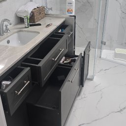 Design flow - Nowoczesna łazienka z szarą szafką pod umywalką z otwartymi szufladami, marmurowym blatem i białą wanną na ozdobnych nóżkach. Widoczne detale armatury i akcesoriów.