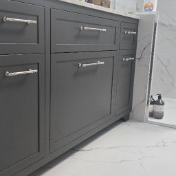 Design flow - Szara szafka łazienkowa z chromowanymi uchwytami na tle marmurowych płytek i kabiny prysznicowej. Minimalistyczny design, nowoczesne wykończenie.