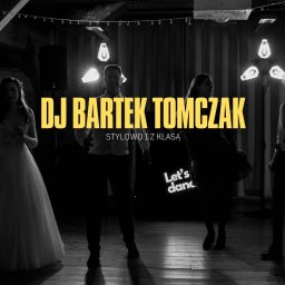 TOMCZAK FOTO BARTOSZ TOMCZAK - Czarno-białe zdjęcie DJ-a Bartka Tomczaka na weselu, oświetlonego lampami, z parą młodą i gośćmi w tle. Napis 'Stylowo i z klasą'.