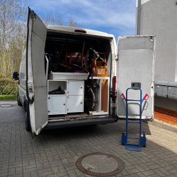 SafeMove - Otwarty furgon załadowany meblami i rowerem, gotowy do przeprowadzki. W tle budynek mieszkalny i wózek transportowy.