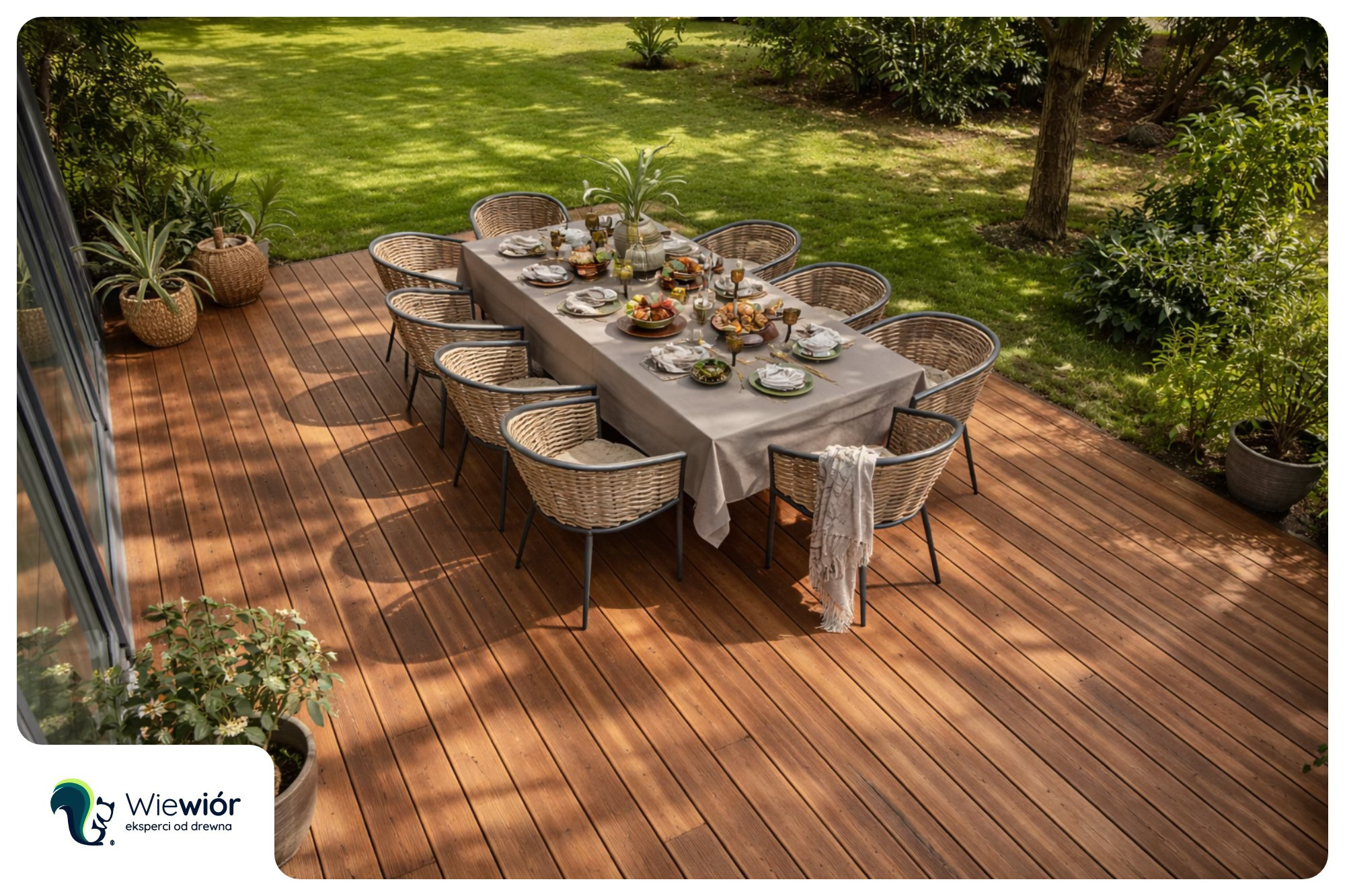 Drewniany taras z kompletem mebli ogrodowych i zastawionym stołem, otoczony zielenią. Widok z góry, ciepłe oświetlenie podkreśla naturalny kolor drewna.