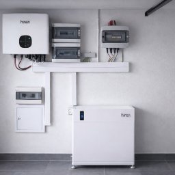 Air Soul Sp. z o.o - Biały magazyn energii Hiren z podłączonym inwerterem i rozdzielnicami na ścianie w pomieszczeniu. Widoczne kable i przewody. Minimalistyczny design.