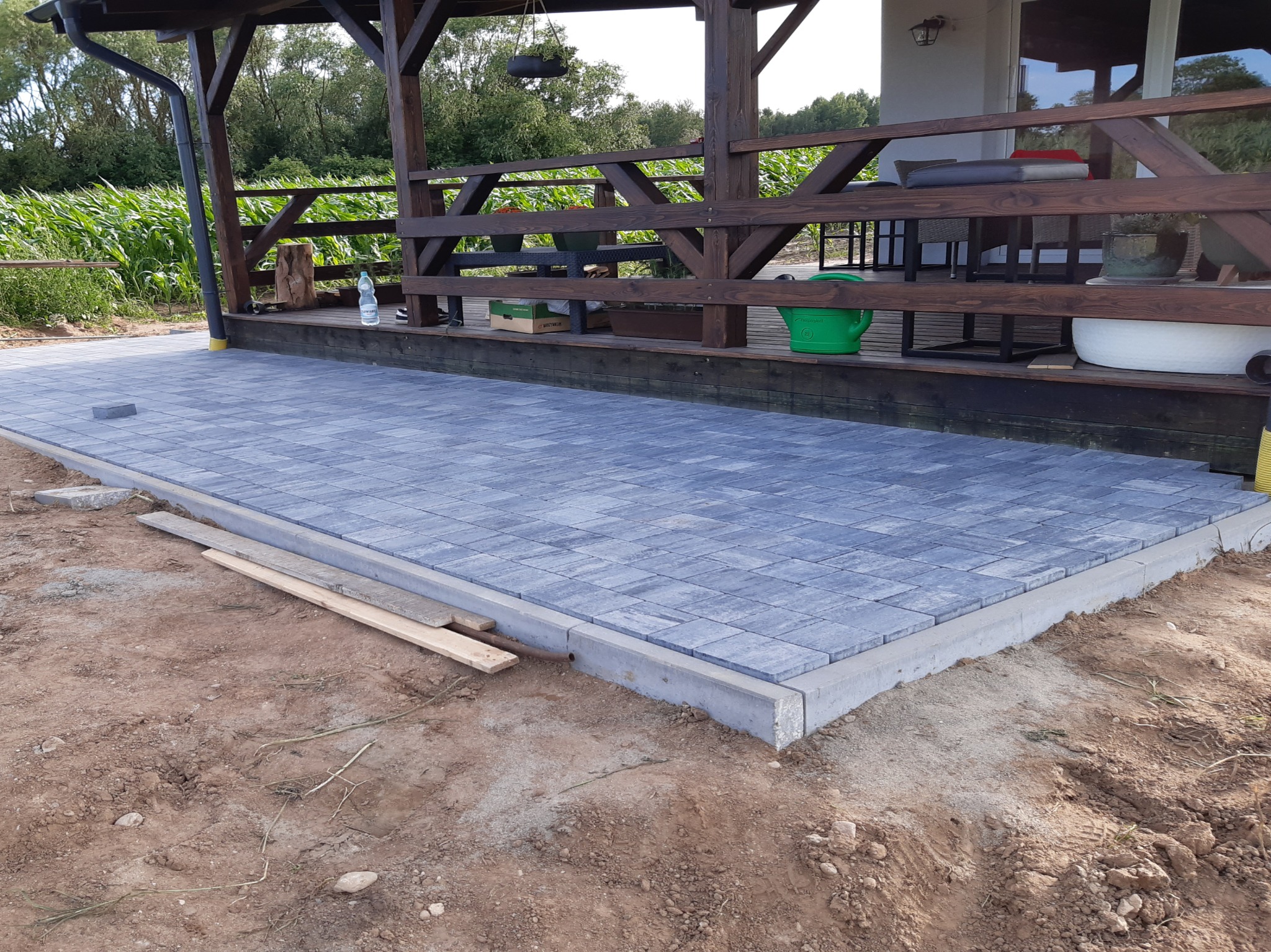 Ułożona kostka brukowa w odcieniach szarości na tarasie z drewnianą konstrukcją zadaszenia. Widoczne elementy wykończeniowe i przygotowany teren.