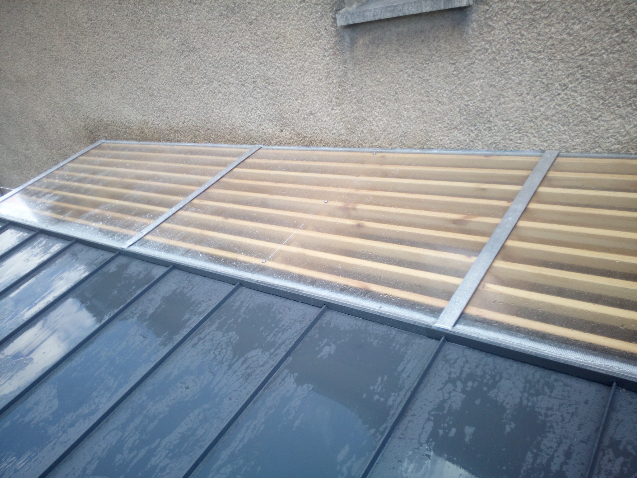 Błyszczący, grafitowy dach z blachy na rąbek stojący, z drewnianą konstrukcją i przezroczystym zadaszeniem, widok z góry, po deszczu.