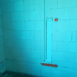 MAR VOLT - Ściana z betonu komórkowego z wyżłobieniami i pomarańczowymi puszkami instalacyjnymi. Pionowy peszel w ścianie. Instalacja elektryczna w trakcie prac.