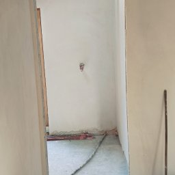 Pro-Tynki - Wnętrze po nałożeniu tynków: gładkie, białe ściany, widoczne instalacje grzewcze podłogowe. Przygotowanie do dalszych prac wykończeniowych.