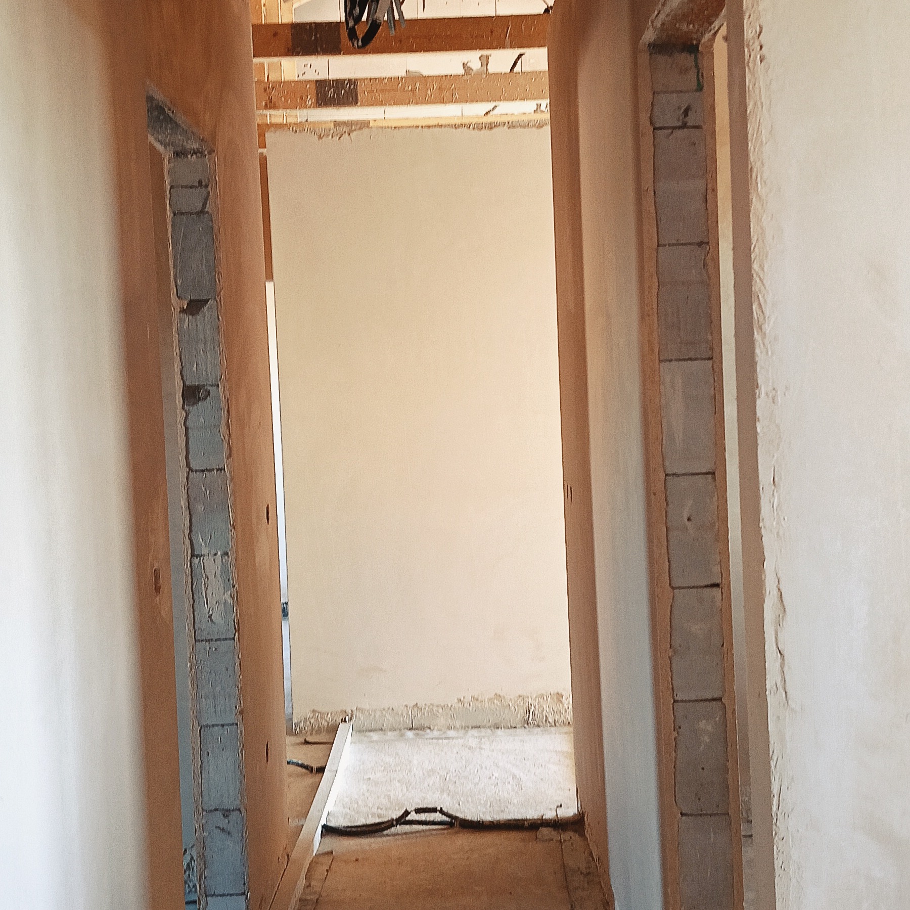 Wnętrze w trakcie prac wykończeniowych: świeżo otynkowane ściany w odcieniach beżu, surowa ościeżnica z bloczków, widok w głąb pomieszczenia.