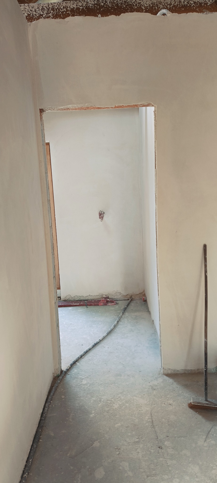 Wnętrze po nałożeniu tynków: gładkie, białe ściany, widoczne instalacje grzewcze podłogowe. Przygotowanie do dalszych prac wykończeniowych.