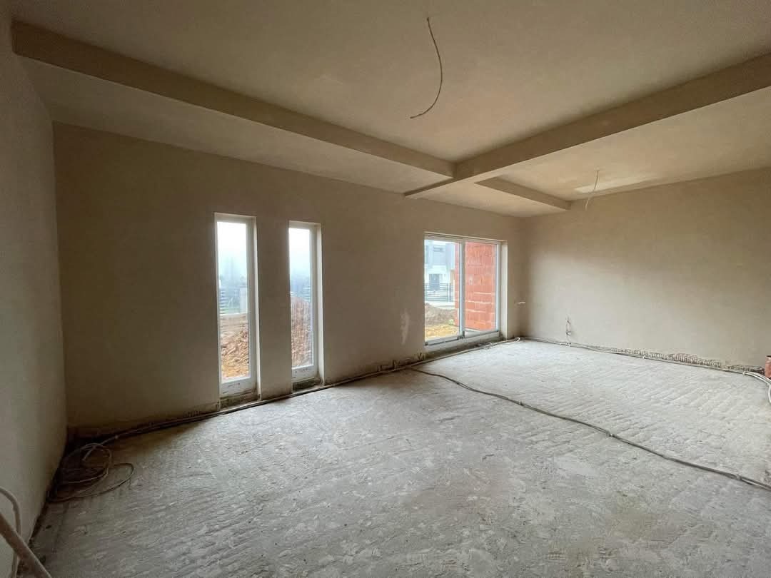 Wnętrze po nałożeniu gładzi gipsowej: ściany i sufit wykończone, widoczne okna i fragment instalacji elektrycznej. Charakterystyczne wykończenie sufitu z podwieszanymi elementami.