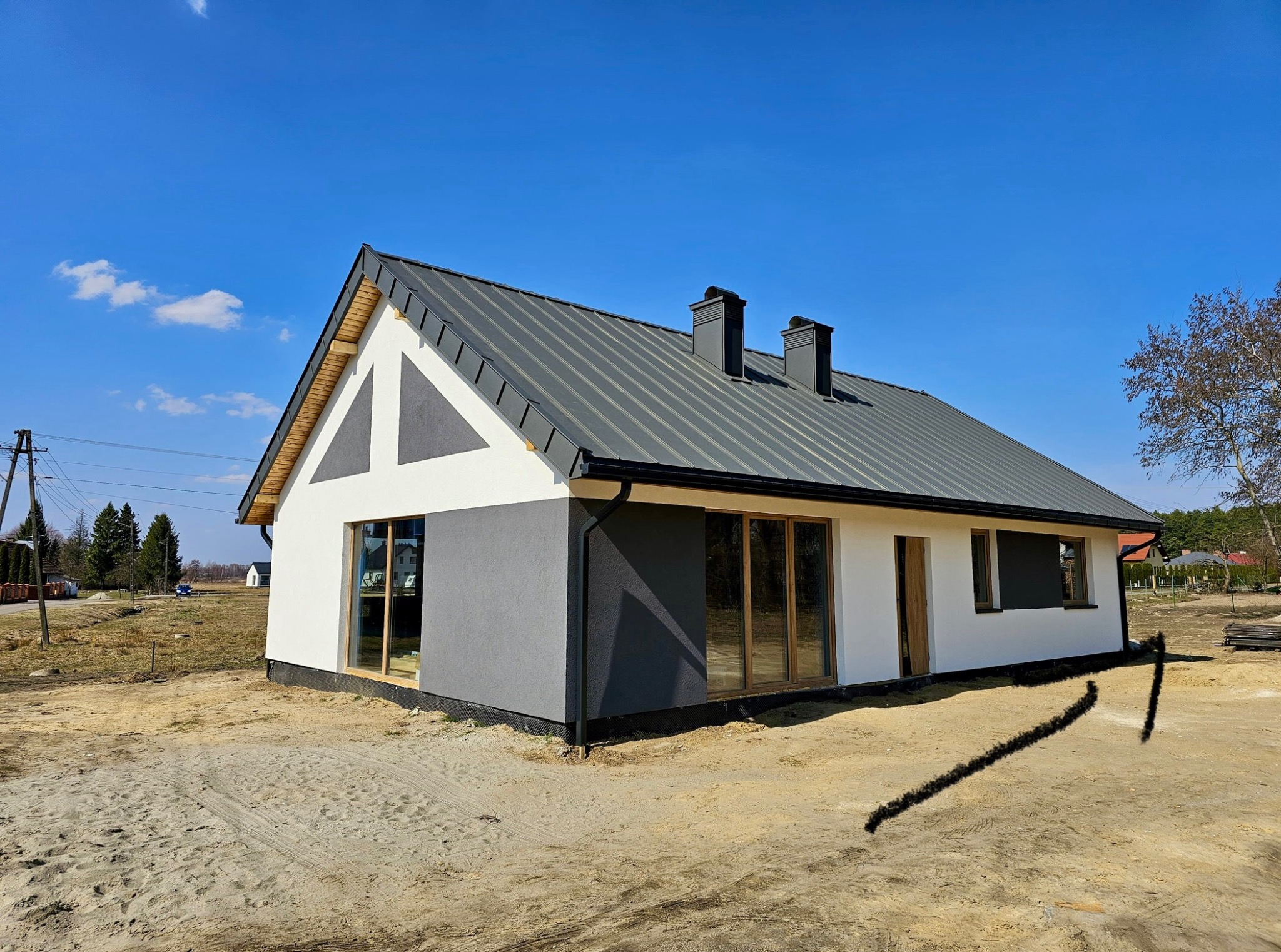 Nowoczesny dom jednorodzinny z szarą blachodachówką i biało-szarą elewacją, widoczny z zewnątrz w słoneczny dzień. Uwagę zwraca dwukolorowa fasada.