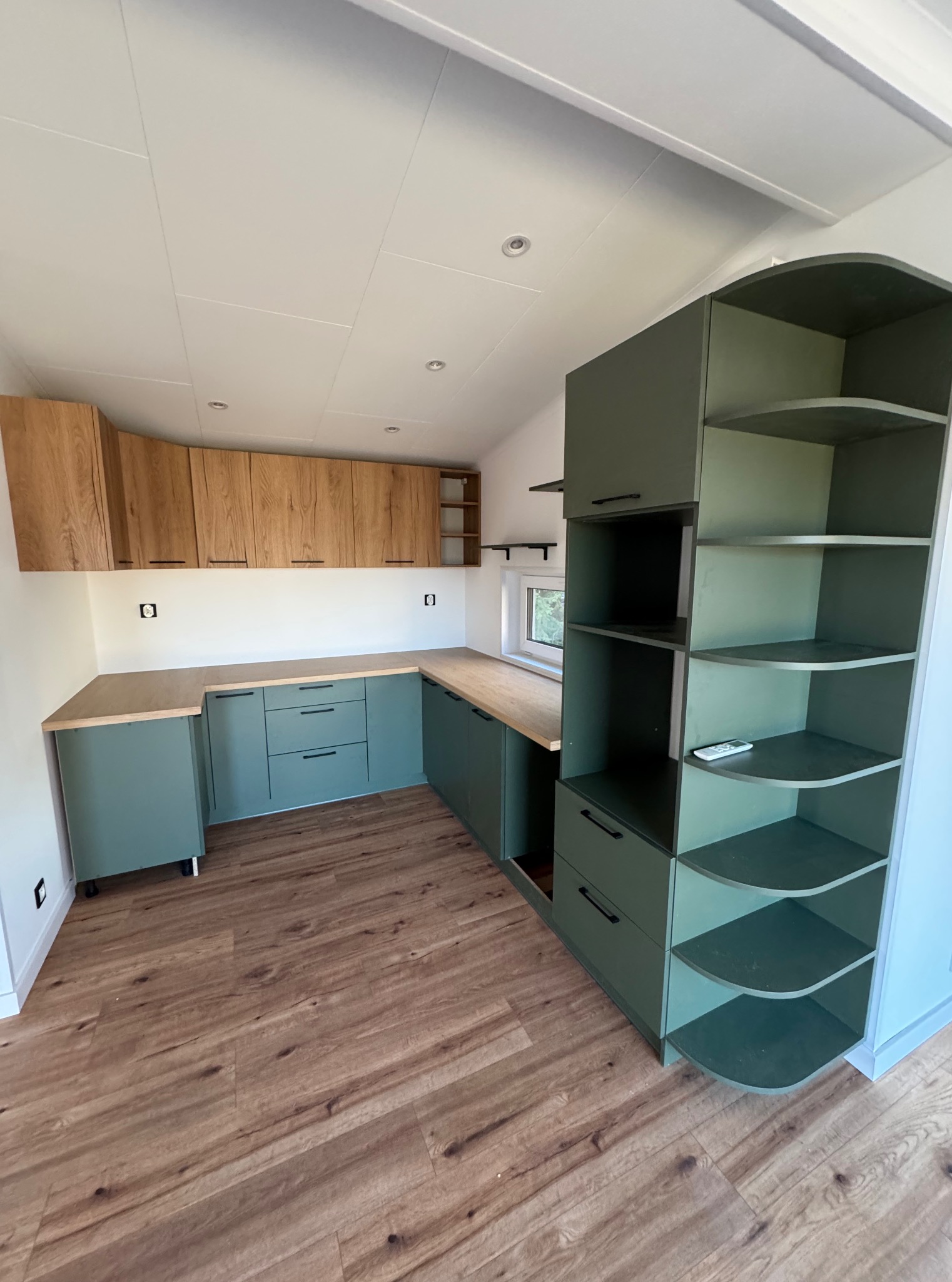 Nowoczesna kuchnia w domu modułowym z drewnianymi i zielonymi szafkami, widok z perspektywy podłogi w Baszni Dolnej. Minimalistyczny design, jasne wnętrze.