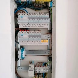 MG Wykonczenia Wnętrz - Rozdzielnica elektryczna Hager w białej obudowie, z precyzyjnie ułożonymi przewodami i zabezpieczeniami. Widoczne listwy zaciskowe i oznaczenia faz. Estetyczny montaż.