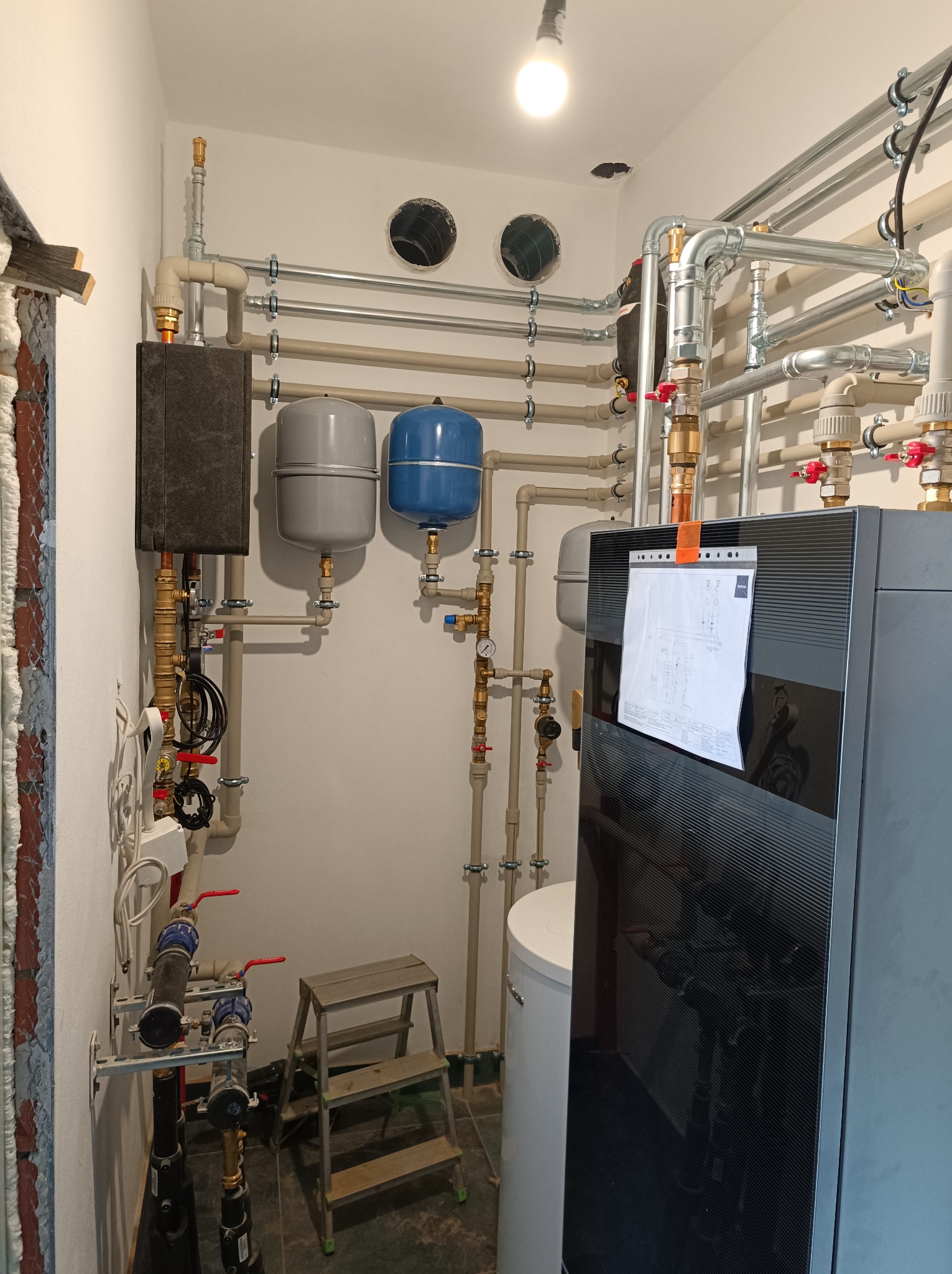 Nowoczesna kotłownia z precyzyjnie ułożonymi rurami, zbiornikami i kotłem. Na kotle widoczny schemat instalacji. Całość oświetlona jasnym światłem.