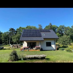 Elektro-Flesz Fotowoltaika oraz Magazyn Energi - Dom jednorodzinny z panelami słonecznymi na dachu, otoczony zielonym trawnikiem i kwiatami. Ujęcie z poziomu ogrodu, w słoneczny dzień.