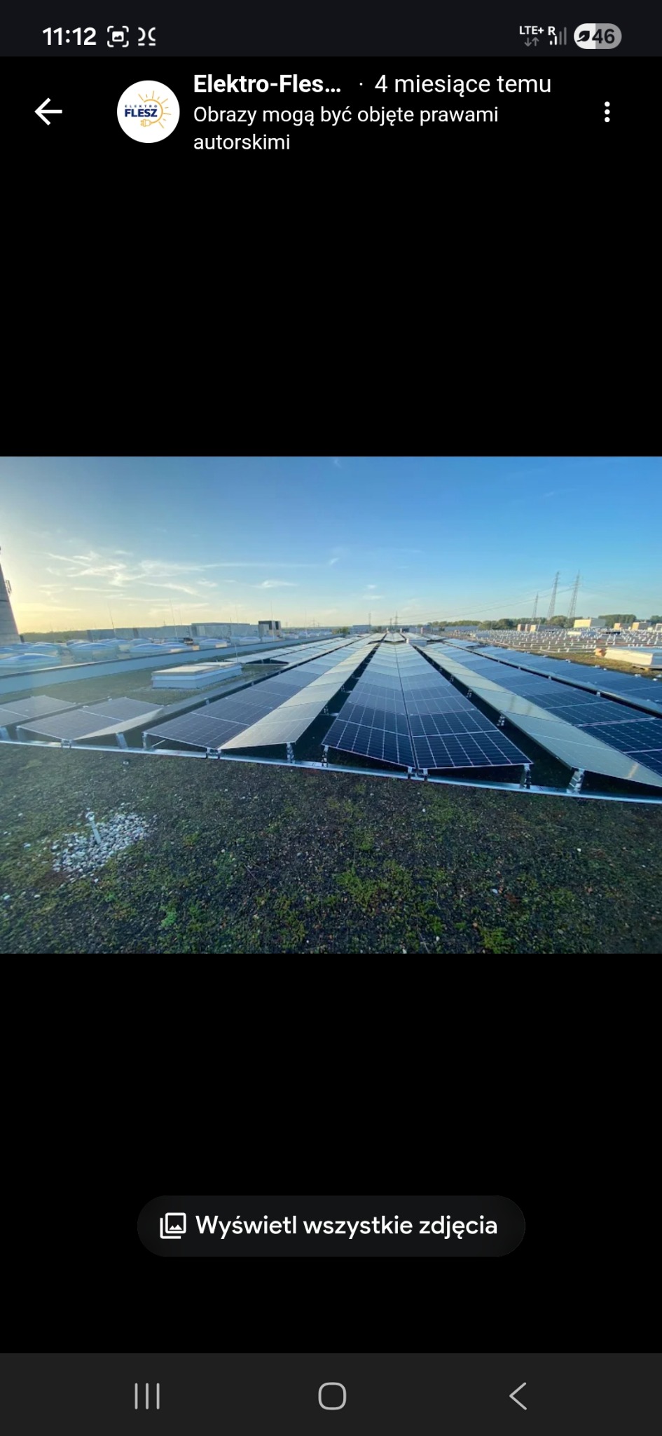 Rozległa instalacja fotowoltaiczna na zielonym dachu budynku, widok z góry, błękitne niebo w tle. Panele ułożone rzędami, równomierne oświetlenie.