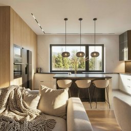 NOVA PRACOWNIA PROJEKTOWA KAROLINA PANFIL-KWIATKOWSKA, ARCHITEKT - Nowoczesna kuchnia z wyspą i salonem w ciepłych barwach. Widok z kanapy na okno z widokiem na zieleń. Minimalistyczne lampy wiszące nad wyspą.