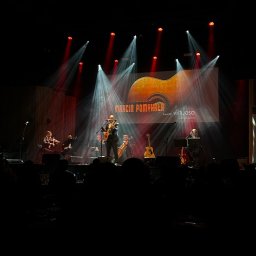 Marcin Pomykała - tenor z gitarą - Zespół muzyczny na scenie podczas koncertu. Wokalista z gitarą, skrzypce, wiolonczela, oświetlenie sceniczne i publiczność w tle. Marcin Pomykała Virtuoso.