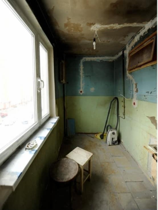 Wnętrze balkonu przed remontem: widoczne ślady po instalacjach elektrycznych na ścianach, brudny sufit, stara podłoga z płytek, krzesła i odkurzacz.