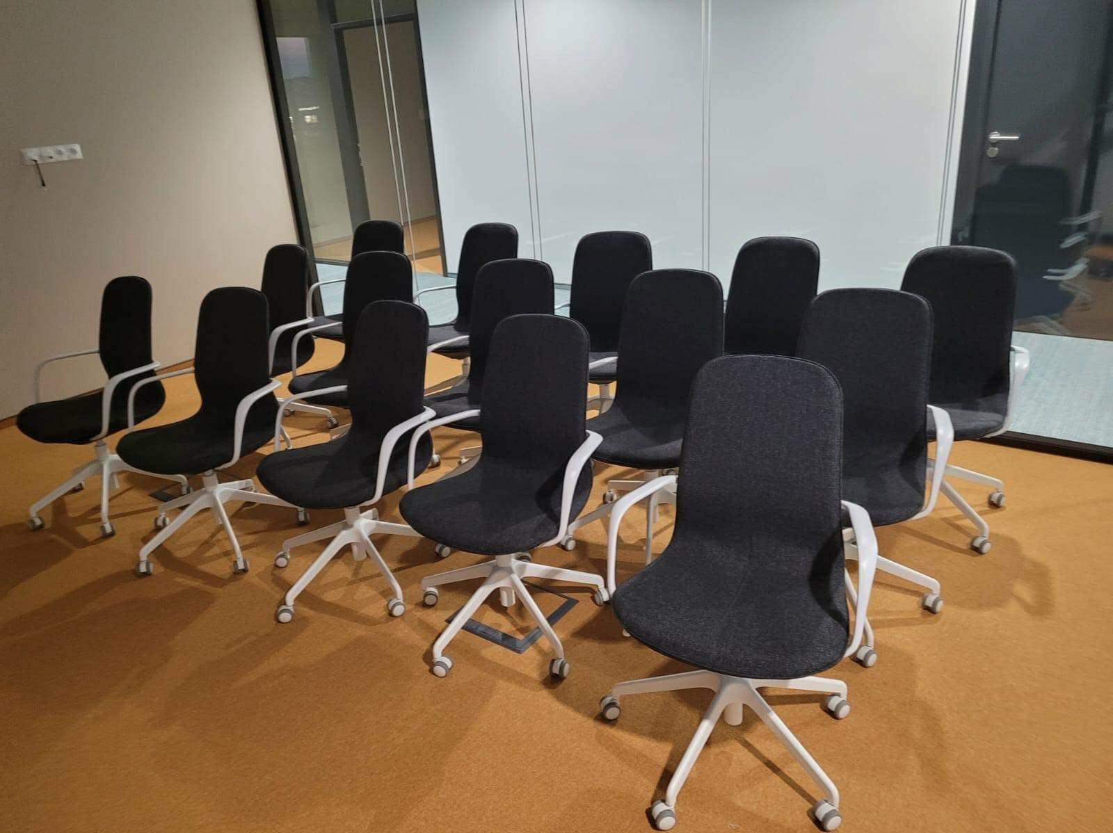 Ustawione krzesła biurowe z szarym obiciem i białymi ramami na kółkach, gotowe do użytku w biurze w Brzegu. Widok z perspektywy podłogi.