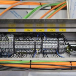 J&M Professional Małgorzata Antyga - Szafa sterownicza z widocznymi listwami zaciskowymi i podłączonymi przewodami w różnych kolorach. Na górze i dole widoczne kable w peszlach.