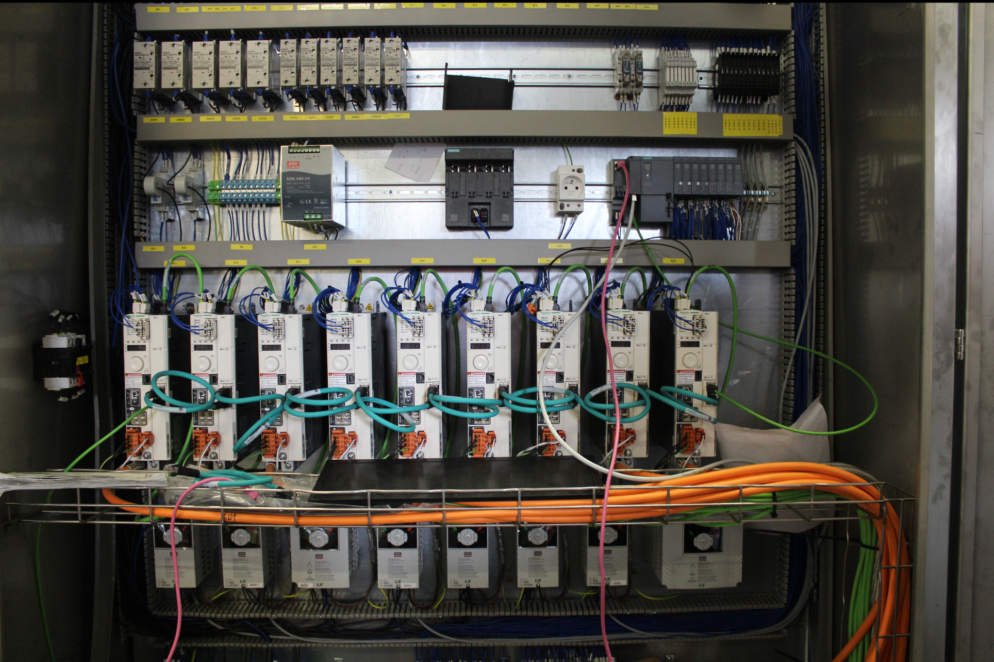 Rozbudowana szafa sterownicza z licznymi modułami, przewodami i złączami, ukazująca zaawansowany system kontroli i dystrybucji energii w przemysłowym otoczeniu.