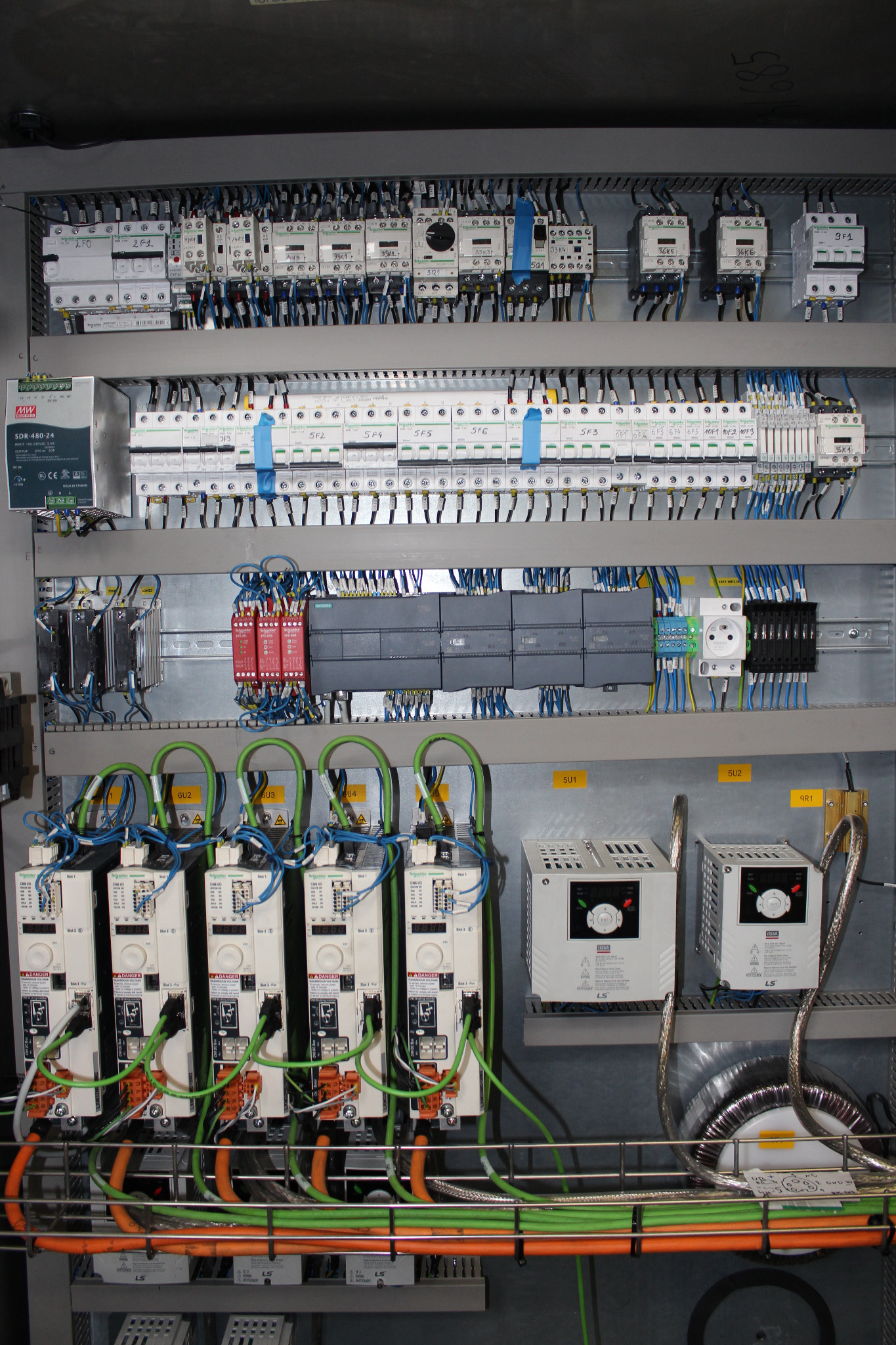 Rozbudowana szafa sterownicza z licznymi elementami elektrycznymi, przewodami i modułami, ukazująca zaawansowany system kontroli i dystrybucji energii w przemysłowym otoczeniu.
