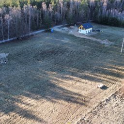 Taxi Wojciech Żuk - Szeroki kadr z drona ukazuje dwa domy w stanie surowym zamkniętym na rozległej działce, otoczone lasem i polami w zimowej scenerii. Widoczne ślady budowy i cień drzew.