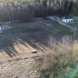 Taxi Wojciech Żuk - Dwa nowoczesne domy jednorodzinne z białymi elewacjami i ciemnymi dachami, widziane z lotu ptaka na tle lasu i zaoranego pola w słoneczny dzień.