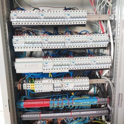 ELEKTRO-SMART Szymon Mazurek - Rozdzielnica elektryczna z licznymi zabezpieczeniami, okablowaniem w różnych kolorach i listwami zaciskowymi, zamontowana w metalowej szafie. Widok z bliska.