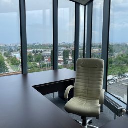 City View Nieruchomości - Agnieszka Sadowska - Nowoczesne biuro z widokiem na miasto przez panoramiczne okna. Biurko z krzesłem biurowym. Minimalistyczny design, jasne wnętrze, przestrzeń do pracy.