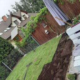 Miłosz Jarosz - Fragment ogrodu z ułożoną trawą, widoczne narzędzia ogrodnicze, ziemia przygotowana pod dalsze prace, w tle dom i ogrodzenie. Ujęcie z boku, lekko z góry.