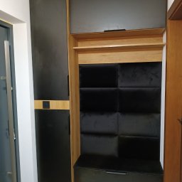 Gajda Meble na wymiar - Nowoczesna szafa wnękowa z czarnymi frontami i drewnianymi akcentami, z siedziskiem i tapicerowanym panelem. Minimalistyczny design, oświetlenie punktowe.