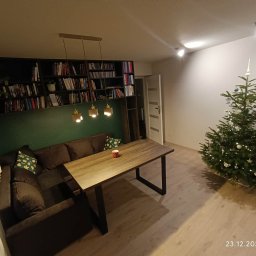 Gajda Meble na wymiar - Nowoczesny salon z narożną sofą, drewnianym stołem na metalowych nogach i regałem na książki w zabudowie. Świąteczny klimat podkreśla choinka z ozdobami.