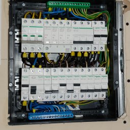 M_Pro_Sys - Rozdzielnica elektryczna Schneider z zabezpieczeniami, widoczne przewody w kolorach: niebieskim, żółtym i zielonym. Instalacja w czarnej obudowie, zamontowana na ścianie.