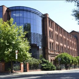 ENGLISH NAVIGATOR SPÓŁKA Z OGRANICZONĄ ODPOWIEDZIALNOŚCIĄ - Budynek szkoły językowej z cegły i szkła, z zielenią w tle. Architektura łączy nowoczesność z tradycją. Widok z ulicy, w słoneczny dzień.