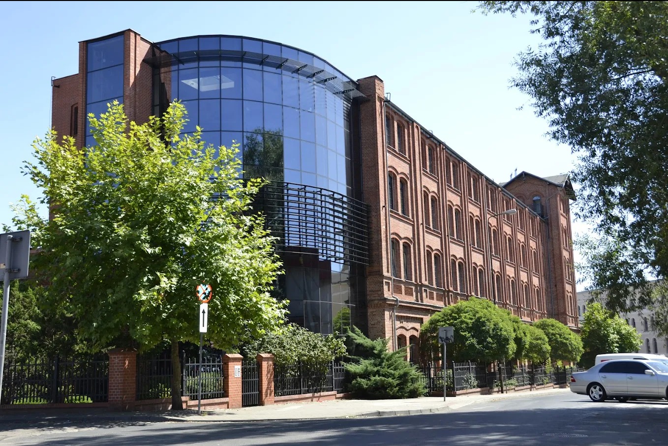 Budynek szkoły językowej z cegły i szkła, z zielenią w tle. Architektura łączy nowoczesność z tradycją. Widok z ulicy, w słoneczny dzień.