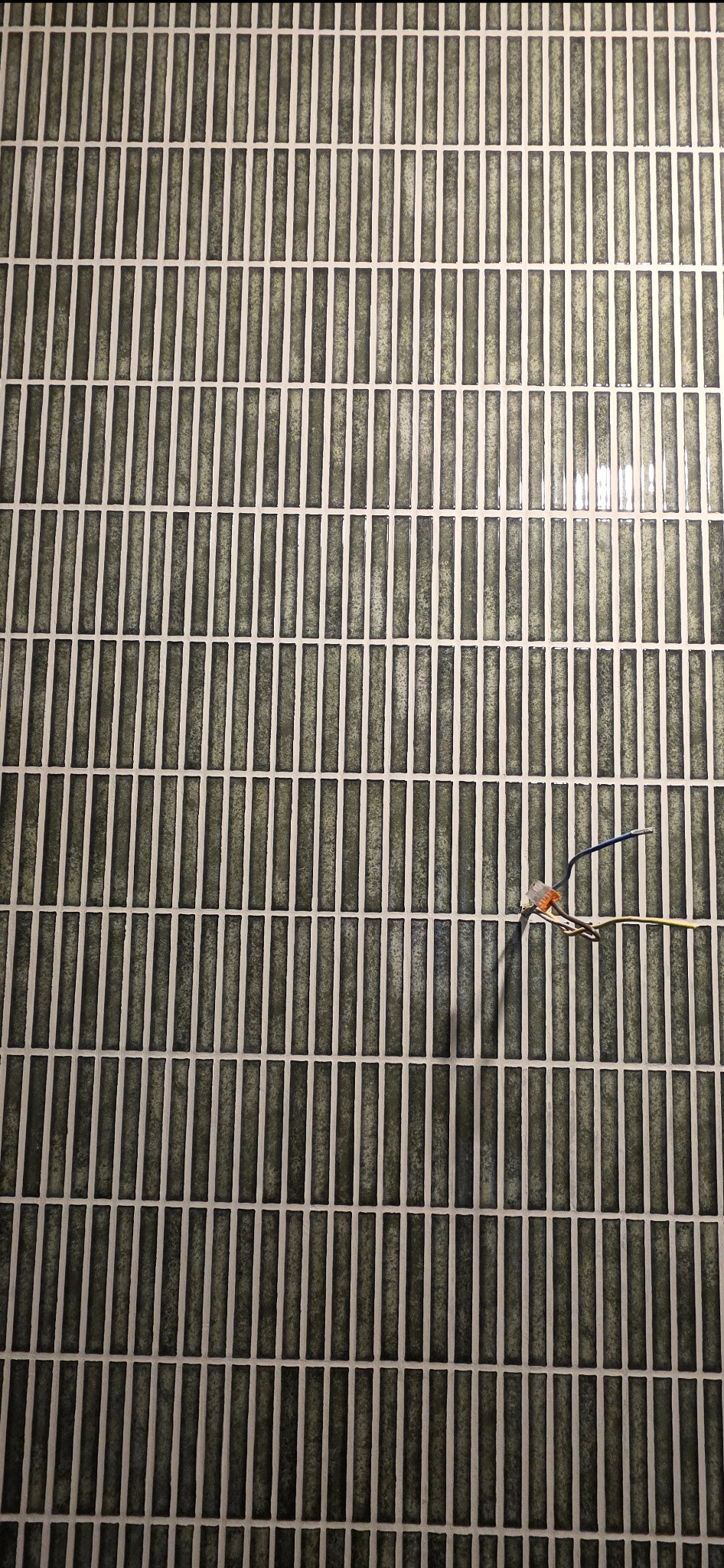 Ułożona, pionowa, zielono-szara mozaika z fugą. Widoczne wystające przewody elektryczne z kostką łączeniową. Nietypowy wzór i kolorystyka płytek.