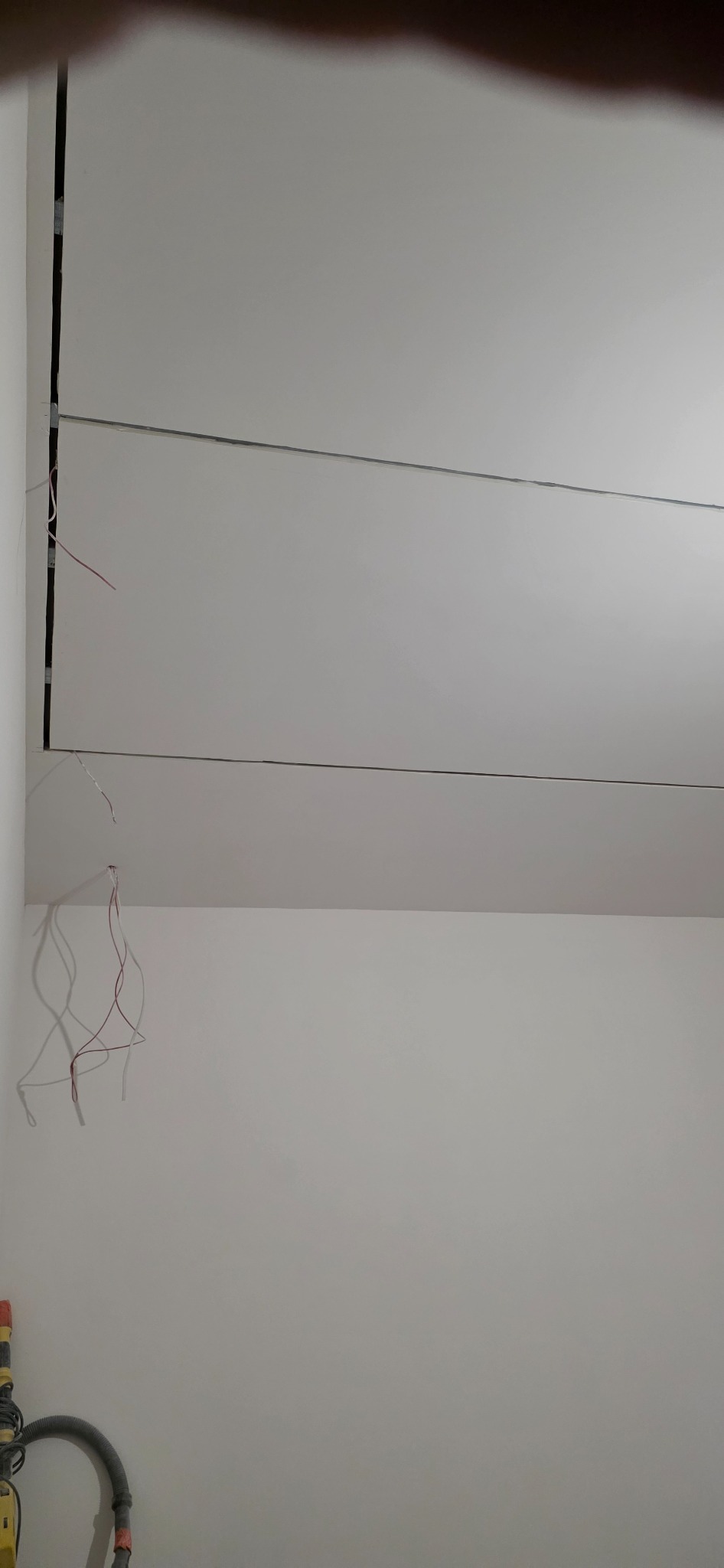 Montaż sufitu podwieszanego z płyt kartonowo-gipsowych, widoczne kable elektryczne i szczelina montażowa. U dołu fragment odkurzacza przemysłowego.