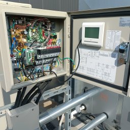 El-Klimbud Szymon Jerzycki - Otwarta szafka sterownicza klimatyzacji z widocznymi przewodami, elektroniką i schematem. Panel sterowania z wyświetlaczem. Widoczne rury instalacyjne.