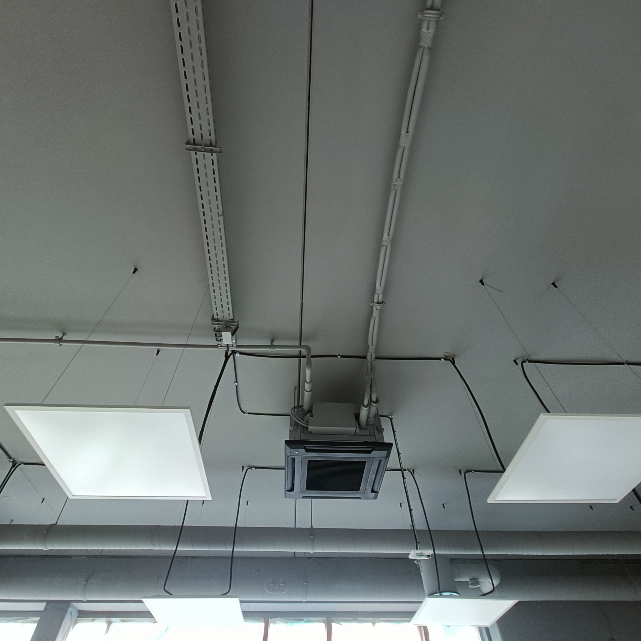 Sufit biurowy z zamontowaną kasetonową klimatyzacją, widoczne kable, rury i oświetlenie LED. Ujęcie z dołu, podkreślające instalacje.