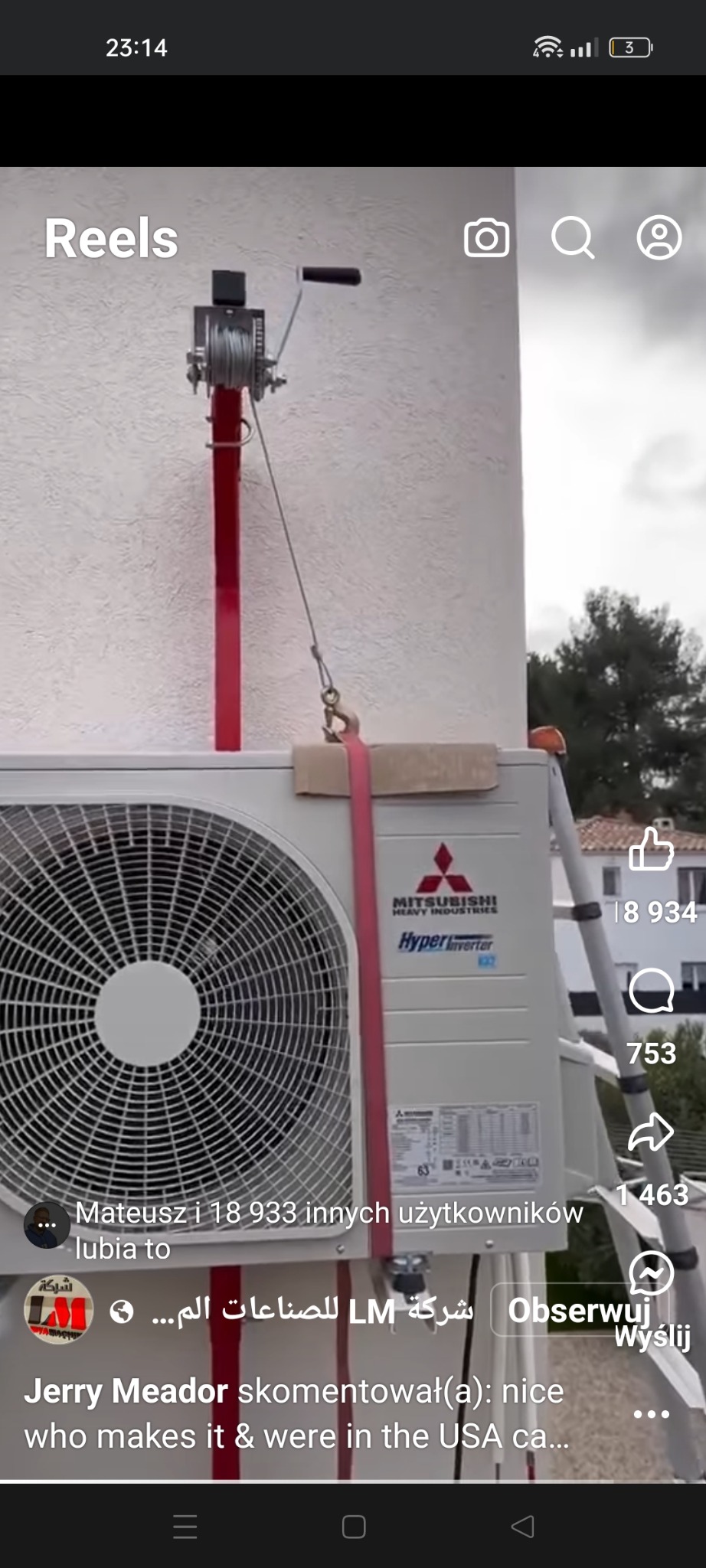 Montaż zewnętrznej jednostki klimatyzacji Mitsubishi na elewacji budynku za pomocą wciągarki linowej. Widoczna drabina i fragment otoczenia.