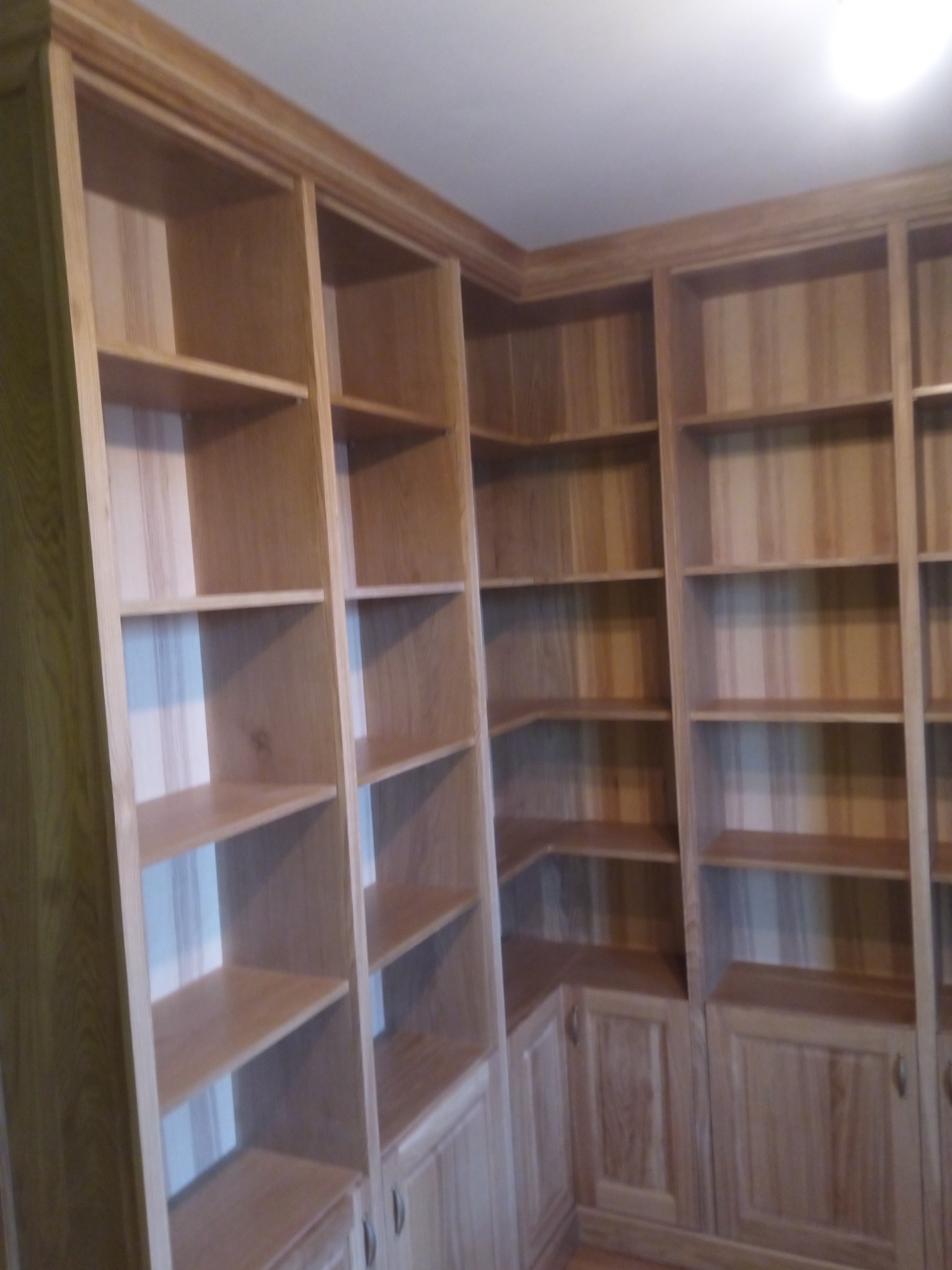 Drewniana zabudowa biblioteczna z półkami i szafkami w dolnej części, wykonana na wymiar, z widocznym wykończeniem w naturalnym odcieniu drewna.