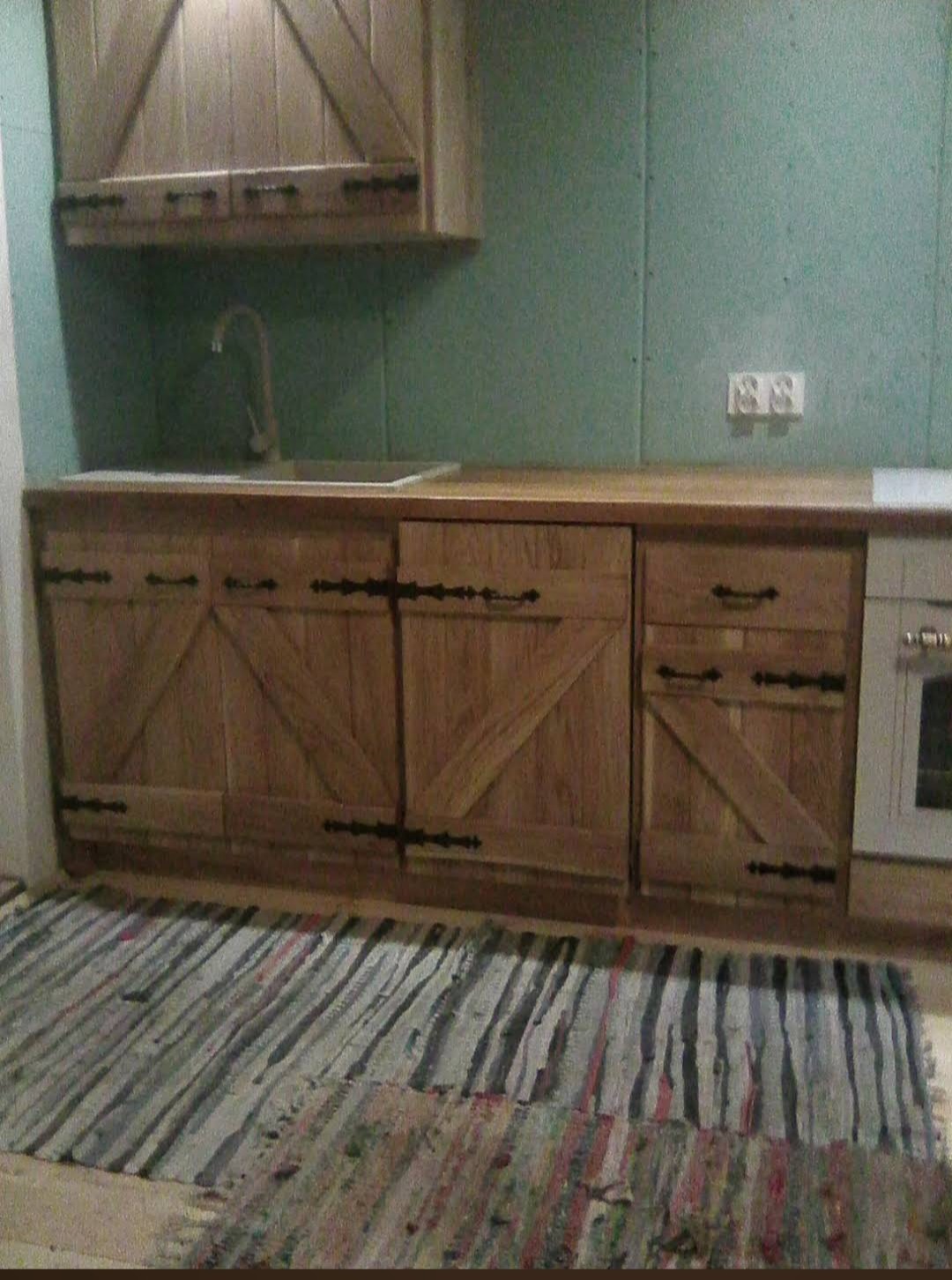 Rustykalna zabudowa kuchenna z drewnianymi frontami w stylu stodoły, z czarnymi zawiasami i uchwytami, uzupełniona o dywanik w paski.